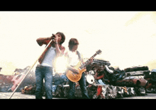 two men singing and playing guitars in front of a pile of junk