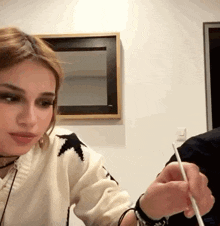 a woman is sitting at a table while a man is holding a chopstick .