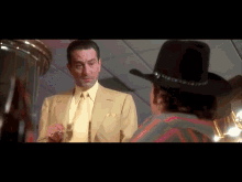a man in a yellow suit and tie is talking to another man in a black cowboy hat