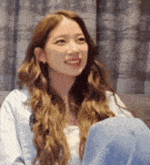 a woman with long brown hair is sitting on a couch and smiling .