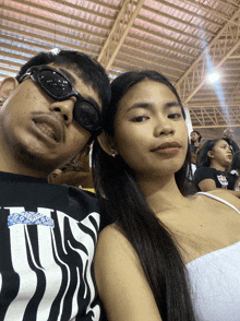 a man and a woman are posing for a picture while the man is wearing sunglasses and the woman is wearing a white top
