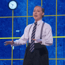 a woman wearing suspenders and a tie stands in front of a blue wall with a clock on it