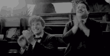 two men are sitting next to each other and clapping their hands .