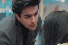 a man in a suit looks at a woman in a black shirt