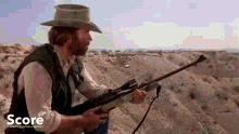 a man in a cowboy hat is holding a gun in the desert .