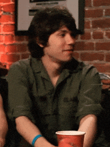 a man wearing a green shirt with the word army on it sits in front of a brick wall
