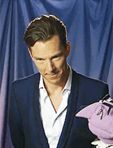 a man in a suit stands next to a purple stuffed animal