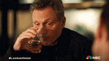 a man drinking a glass of whiskey with the nbc logo in the corner