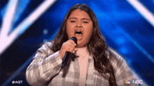 a girl is singing into a microphone on a stage with a nbc logo in the background
