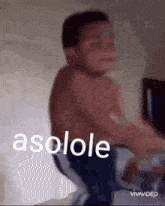 a shirtless boy is sitting on a bed with the word asolole written on the bottom of the image .