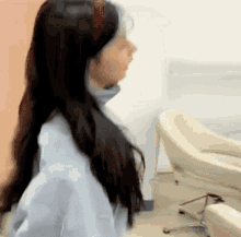 a woman with long black hair is standing in a room with a chair .