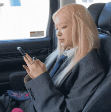 a woman in a suit sits in a car looking at her phone