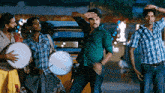 a man in a green shirt is dancing in front of a group of men holding drums