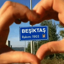 a person making a heart shape with their hands in front of a blue sign that says besiktas