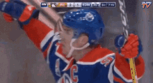 a hockey player in a red white and blue uniform is holding a hockey stick in front of a screen that says oilers tv
