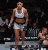 a woman in a ufc top and shorts stands in a boxing ring