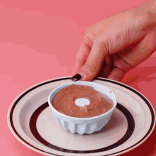 a hand is reaching for a small bowl of chocolate pudding on a plate