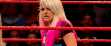 a woman in a pink outfit is standing in a wrestling ring with a crowd behind her .
