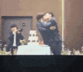 two men are kissing in front of a wedding cake while a man takes a picture .