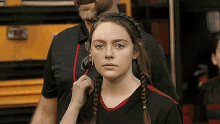 a girl with braids is standing next to a man in front of a school bus .