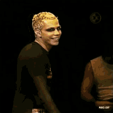 a man with blonde hair is smiling in a dark room while wearing a black shirt .