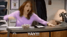 a woman is yawning while sitting at a desk in an office with her mouth open .