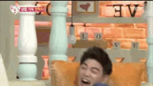 a man is laughing while sitting on a couch in front of a sign that says love .