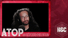a man with glasses and a beard is sitting in front of a microphone with the name atop on the bottom