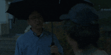 a man in a blue shirt holds an umbrella over another man