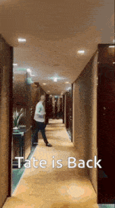 a man is walking down a hallway with the words tate is back written on the bottom