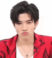 a young man wearing a red jacket and a necklace is making a face .