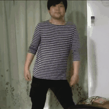 a man wearing a striped shirt and black pants stands in front of a white curtain