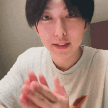 a young man wearing a white t-shirt is clapping his hands together