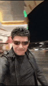 a man wearing sunglasses and a leather jacket takes a picture of himself