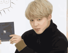 a young man with blonde hair is wearing a black turtleneck sweater and holding a cd .