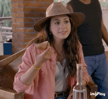 a woman wearing a hat and a pink shirt is eating a piece of bread