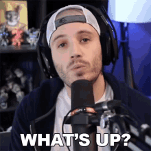 a man wearing headphones stands in front of a microphone with the words what 's up written below him