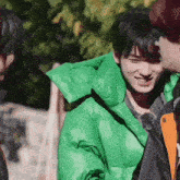 a man wearing a green jacket is smiling while standing next to two other men .