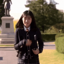a young girl in a school uniform is standing in front of a statue
