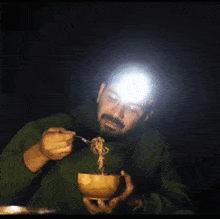 a man in a green shirt is eating from a wooden bowl