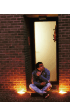 a man sits on the ground in front of a door with candles on the ground