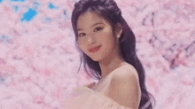 a woman in a pink dress is standing in front of a cherry blossom tree and smiling .