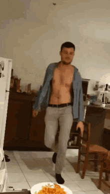 a shirtless man is walking in a kitchen next to a plate of spaghetti