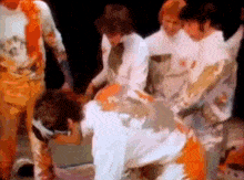 a group of men are covered in orange paint and standing next to each other on a stage .