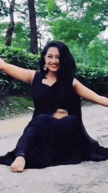 a woman in a black dress sits on the ground with her arms outstretched