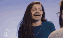 a man with long hair is wearing a blue sweater with a zodiac sign that says gemini