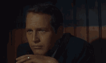 a man in a suit and tie with a ring on his finger is sitting in a dark room .