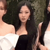 three women are standing next to each other in front of a green plant .
