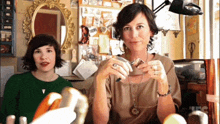two women are sitting in front of a mirror with the letters jfc on the bottom right