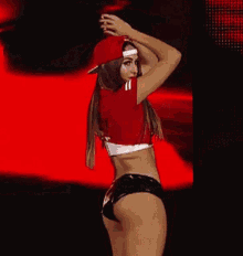 a woman in a red shirt and black shorts is standing on a stage in front of a red background .